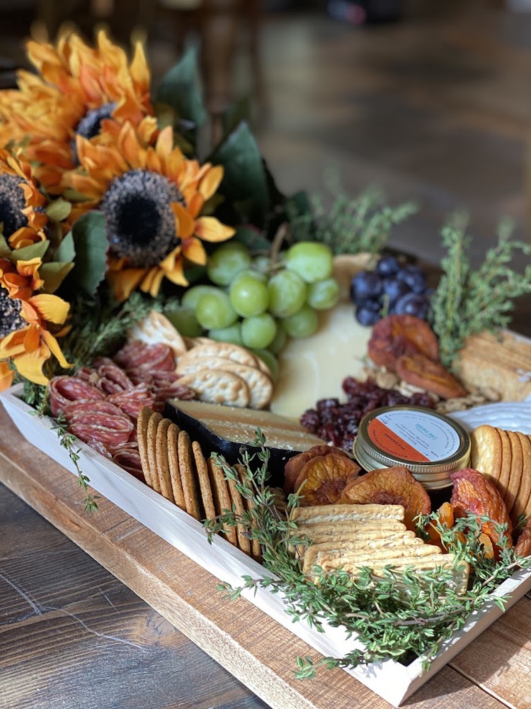 A fall grazing tray with sunflowers, salami, aged gouda, dried peaches, and a jar of honey, photographed in the shoppe